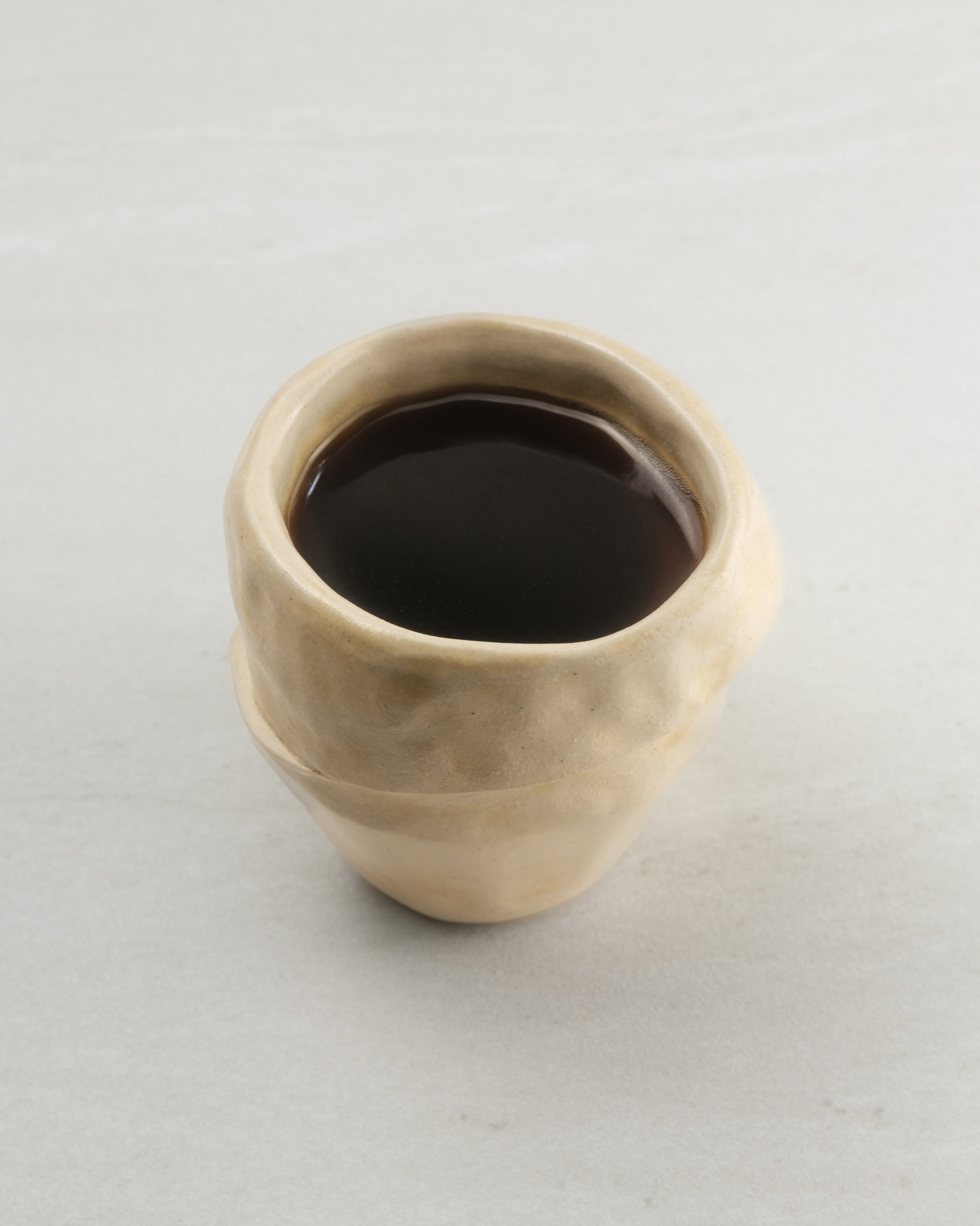 Small beige ceramic cup filled with dark liquid on a light gray background